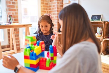 Beautiful teacher and toddler girl playing with construction blocks bulding tower at kindergarten