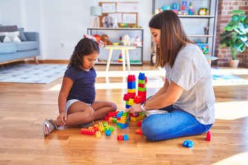 Beautiful teacher and toddler girl playing with construction blocks bulding tower at kindergarten