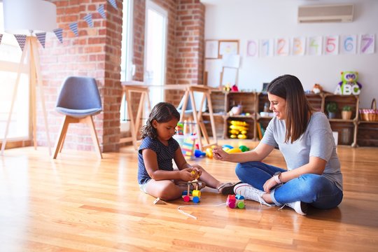 Beautiful teacher and toddler girl playing with train at kindergarten