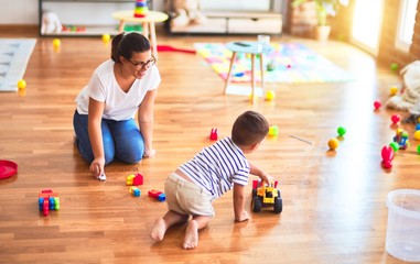 Fototapeta premium Beautiful teacher and toddler boy playing with tractor and cars at kindergarten