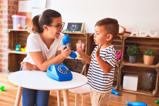 Beautiful teacher and toddler boy playing with vintage blue phone at kindergarten