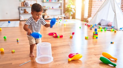Beautiful toddler boy playing drum using skitlle and plastic basket at kindergarten