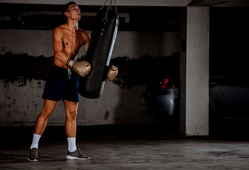 Man practicing boxing on big black bag in garage