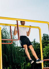 Fototapeta premium Man shakes his muscles on bar in city park. Crossfit concept