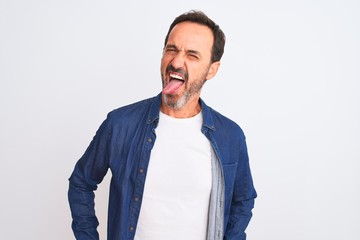 Middle age handsome man wearing blue denim shirt standing over isolated white background sticking tongue out happy with funny expression. Emotion concept.