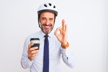 Middle age businessman wearing bike helmet drinking coffee over isolated white background doing ok sign with fingers, excellent symbol
