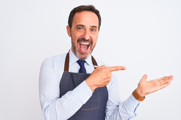 Middle age shopkeeper man wearing apron standing over isolated white background amazed and smiling to the camera while presenting with hand and pointing with finger.