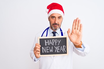 Senior doctor man wearing christmas hat holding blackboard over isolated white background with open hand doing stop sign with serious and confident expression, defense gesture