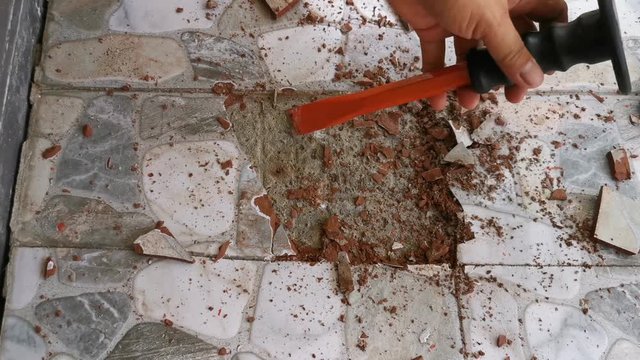 club hammer hitting a bolster chisel, to loosen a piece of tile fixed to a floor.