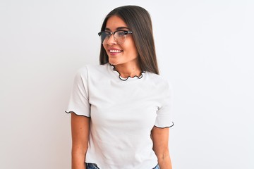 Young beautiful woman wearing casual t-shirt and glasses over isolated white background looking away to side with smile on face, natural expression. Laughing confident.