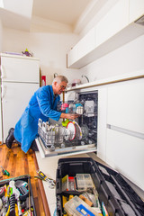 Old age workman is opening the dishwashers with a bunch of tools near him