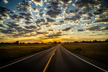 Paved Road leading into the Horizon as sun rays beam out of the clouds
