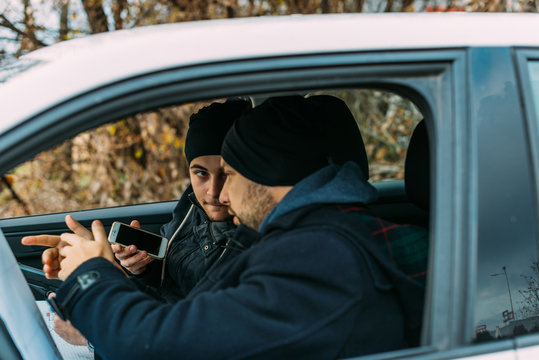 Two Thieves parked in an ally waiting while talking on the phone, observing their target and loading their guns.