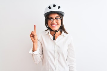 Beautiful businesswoman wearing glasses and bike helmet over isolated white background showing and pointing up with finger number one while smiling confident and happy.