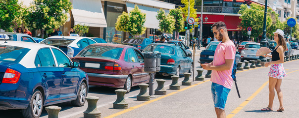 Fototapeta premium Student calling a taxi while wearing a backpack on his shoulder and standing on a city boardwalk.
