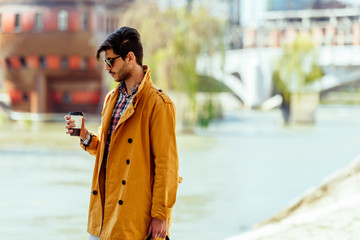 Fashionable businessman walking on city sqaure while holding coffee