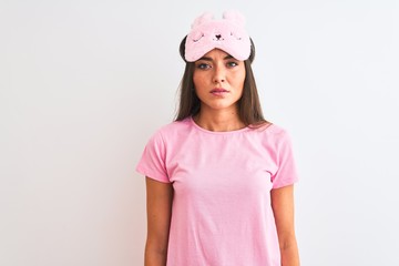 Young beautiful woman wearing sleep mask standing over isolated white background with serious expression on face. Simple and natural looking at the camera.