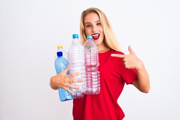 Young beautiful woman recycling plastic bottles standing over isolated white background very happy pointing with hand and finger