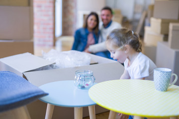 Beautiful family sitting on the floor playing with his kid at new home around cardboard boxes