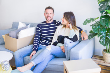 Obraz premium Young beautiful couple sitting on the sofa drinking cup of coffee at new home around cardboard boxes