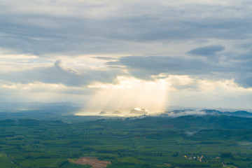 Sunlight of sunset shine through space between clouds above the mountains and the ground. Trang, Thailand.