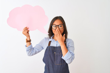 Chinese woman wearing glasses apron holding speech bubble over isolated white background cover mouth with hand shocked with shame for mistake, expression of fear, scared in silence, secret concept