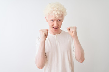 Young albino blond man wearing casual t-shirt standing over isolated white background celebrating surprised and amazed for success with arms raised and open eyes. Winner concept.