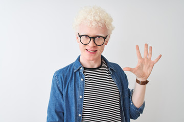 Young albino blond man wearing denim shirt and glasses over isolated white background showing and pointing up with fingers number five while smiling confident and happy.