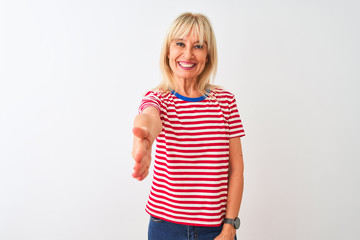 Middle age woman wearing casual striped t-shirt standing over isolated white background smiling friendly offering handshake as greeting and welcoming. Successful business.