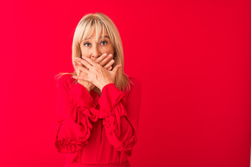 Middle age woman wearing elegant shirt standing over isolated red background shocked covering mouth with hands for mistake. Secret concept.