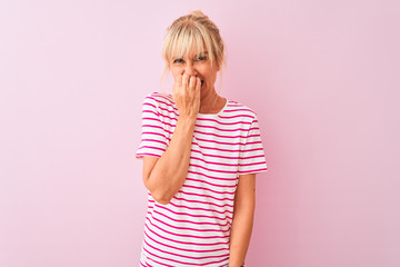 Middle age woman wearing striped t-shirt standing over isolated pink background looking stressed and nervous with hands on mouth biting nails. Anxiety problem.