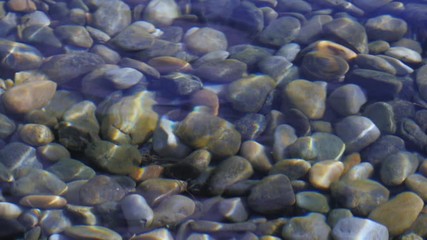 Reflective smooth water glistens with pebbles under promoting peace, zen and harmony, slow motion.