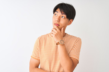 Young chinese man wearing casual striped t-shirt standing over isolated white background with hand on chin thinking about question, pensive expression. Smiling with thoughtful face. Doubt concept.