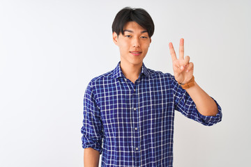 Young chinese man wearing casual blue shirt standing over isolated white background showing and pointing up with fingers number two while smiling confident and happy.