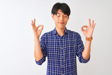 Young chinese man wearing casual blue shirt standing over isolated white background relax and smiling with eyes closed doing meditation gesture with fingers. Yoga concept.