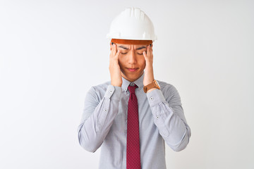 Chinese architect man wearing tie and helmet standing over isolated white background with hand on head for pain in head because stress. Suffering migraine.