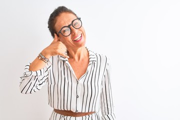 Middle age businesswoman wearing striped dress and glasses over isolated white background smiling doing phone gesture with hand and fingers like talking on the telephone. Communicating concepts.