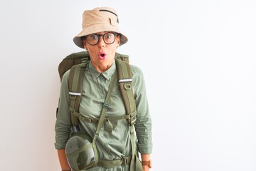 Middle age hiker woman wearing backpack canteen hat glasses over isolated white background afraid and shocked with surprise expression, fear and excited face.