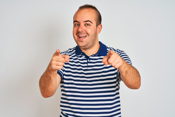 Young man wearing casual striped polo standing over isolated white background pointing to you and the camera with fingers, smiling positive and cheerful