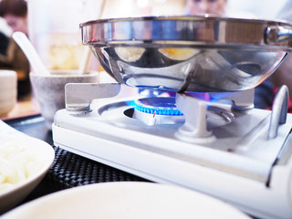 gas stove with blue flames of burning gas under shabu shabu stainless steel pot