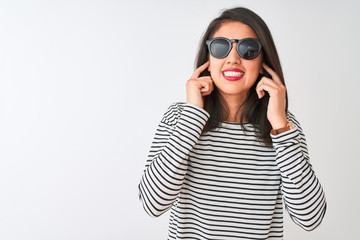 Naklejka premium Chinese woman wearing striped t-shirt and sunglasses standing over isolated white background covering ears with fingers with annoyed expression for the noise of loud music. Deaf concept.