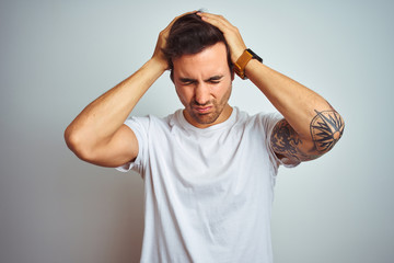 Fototapeta na wymiar Young handsome man with tattoo wearing casual t-shirt over isolated white background suffering from headache desperate and stressed because pain and migraine. Hands on head.