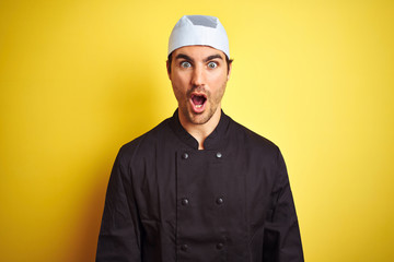 Young handsome chef man cooking wearing uniform and hat over isolated yellow background afraid and...