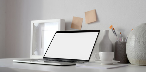 Minimal workspace with open blank screen laptop computer and mock up frame on white table
