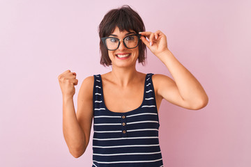 Beautiful woman wearing striped t-shirt and glasses standing over isolated pink background screaming proud and celebrating victory and success very excited, cheering emotion