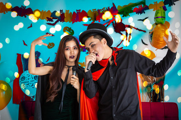 Wizard man and witch woman singing karaoke blue white background with decoration - Asian young people in halloween party concept