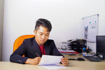 Young Asian man in office writing and reading a paperwork, or sign a contract in casual outfit