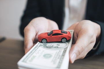 Car salespeople are submitting cash with model cars to customers with concept of buying a new car.