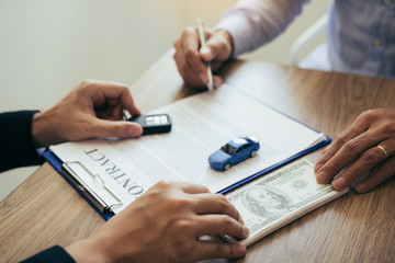 New car buyers are signing a contract with a car salesman at the showroom on the day of receiving the car and handing cash to the employee.