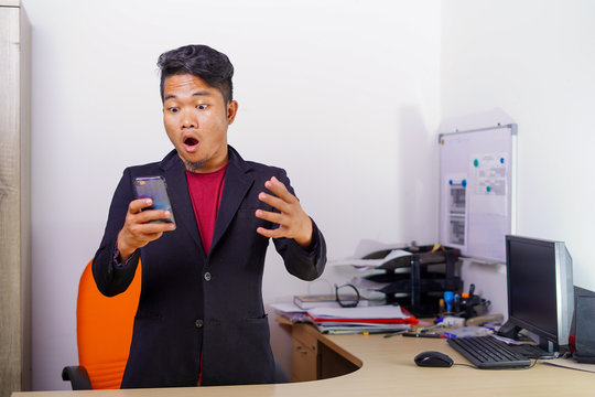 Young Asian man with excited, happiness, surprised face expression sitting or standing up in office, casual suit outfit, successful man achieve the goal.